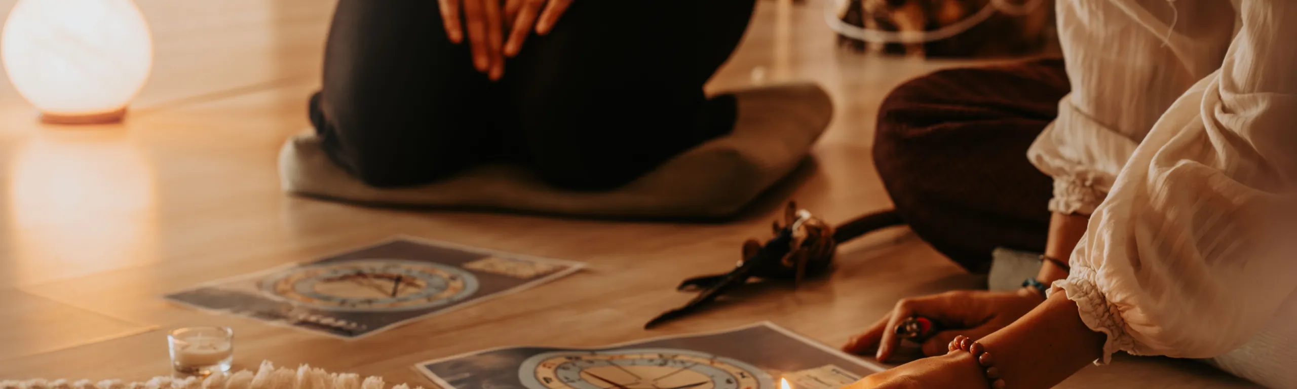 Au sol d’une salle d’atelier : un tapis fleuri, des cartes du ciel imprimées et une bougie allumée, entre deux personnes assises.